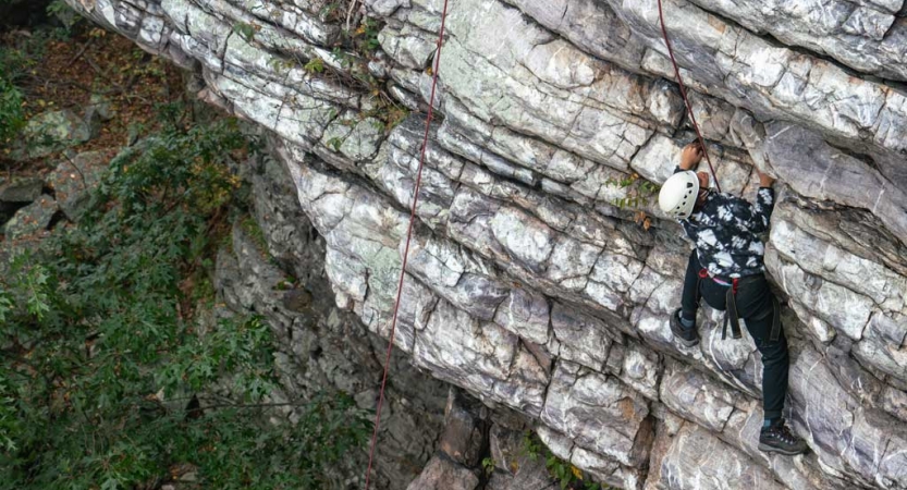 a person wearing safety gear scales a rock wall on a rock climbing trip with outward bound